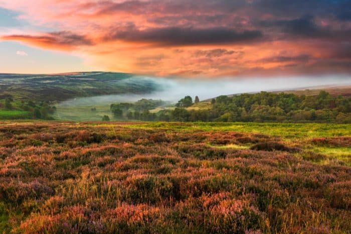 Scenic view of rolling hills and moorland at sunset with colourful sky and mist.