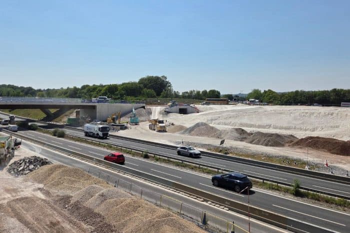 Road construction with machinery and vehicles on a motorway near a bridge.