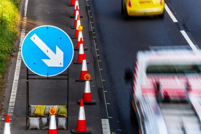 A lane closure with cones and diversion signage on a busy road.